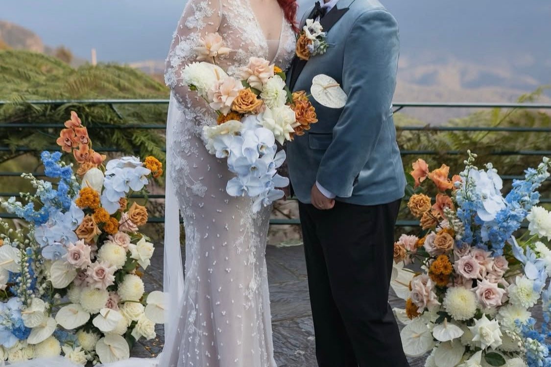 Couple kissing in front of a scenic backdrop with mountains and flowers.