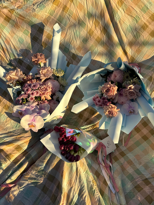Two bouquets of flowers, one with purple and the other with pink as the main colors, both wrapped in blue paper with ribbon.