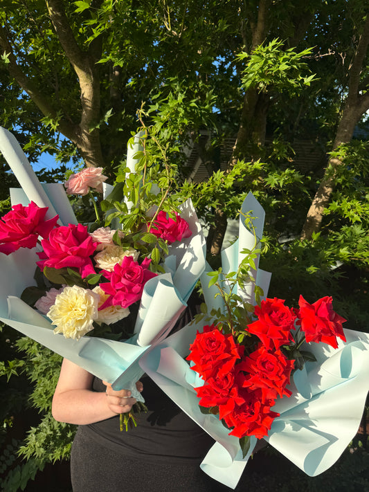 A bouquet of various flowers including pink, red, and white, held in front of a blurred greenery background.